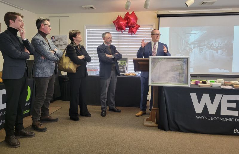 Executives speak at a podium in a conference room, with balloons in the background.