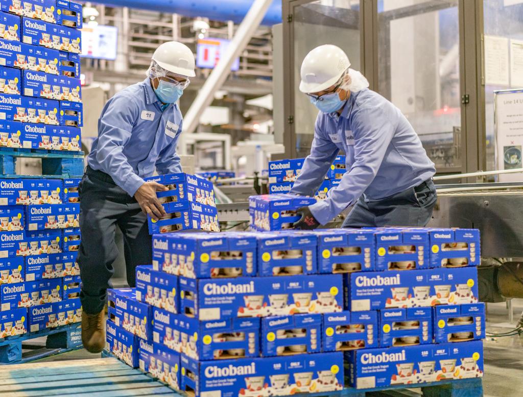Chobani employees lift boxes onto a palette inside a factory.
