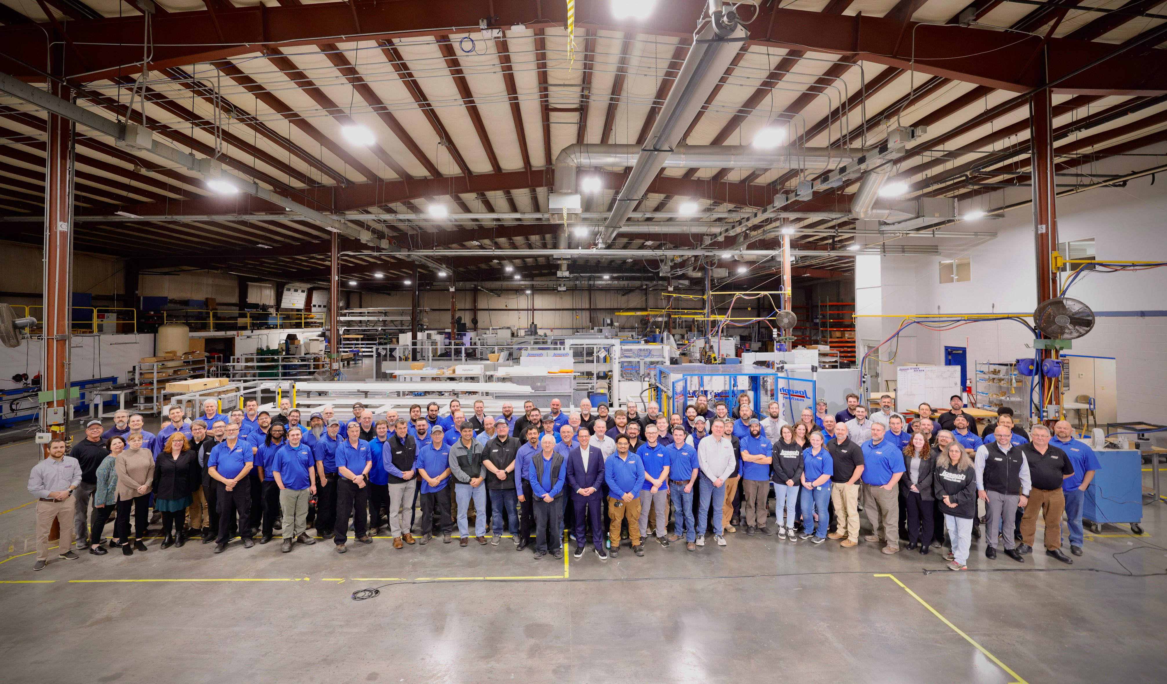 A large group of factory works, Gov. Shapiro, and Sec. Rick Siger, pose for a group photo in a manufacturing facility.