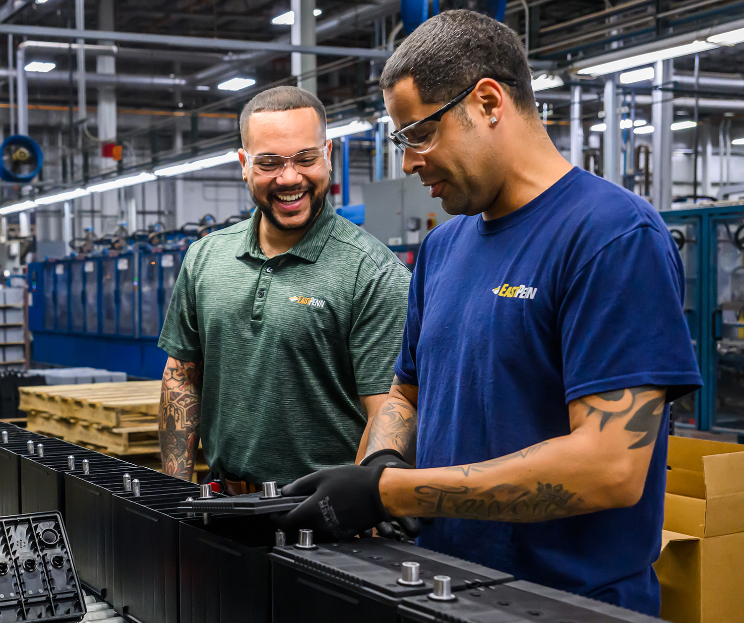 Two manufacturing facility workers pose for a photo while working on an assembly line