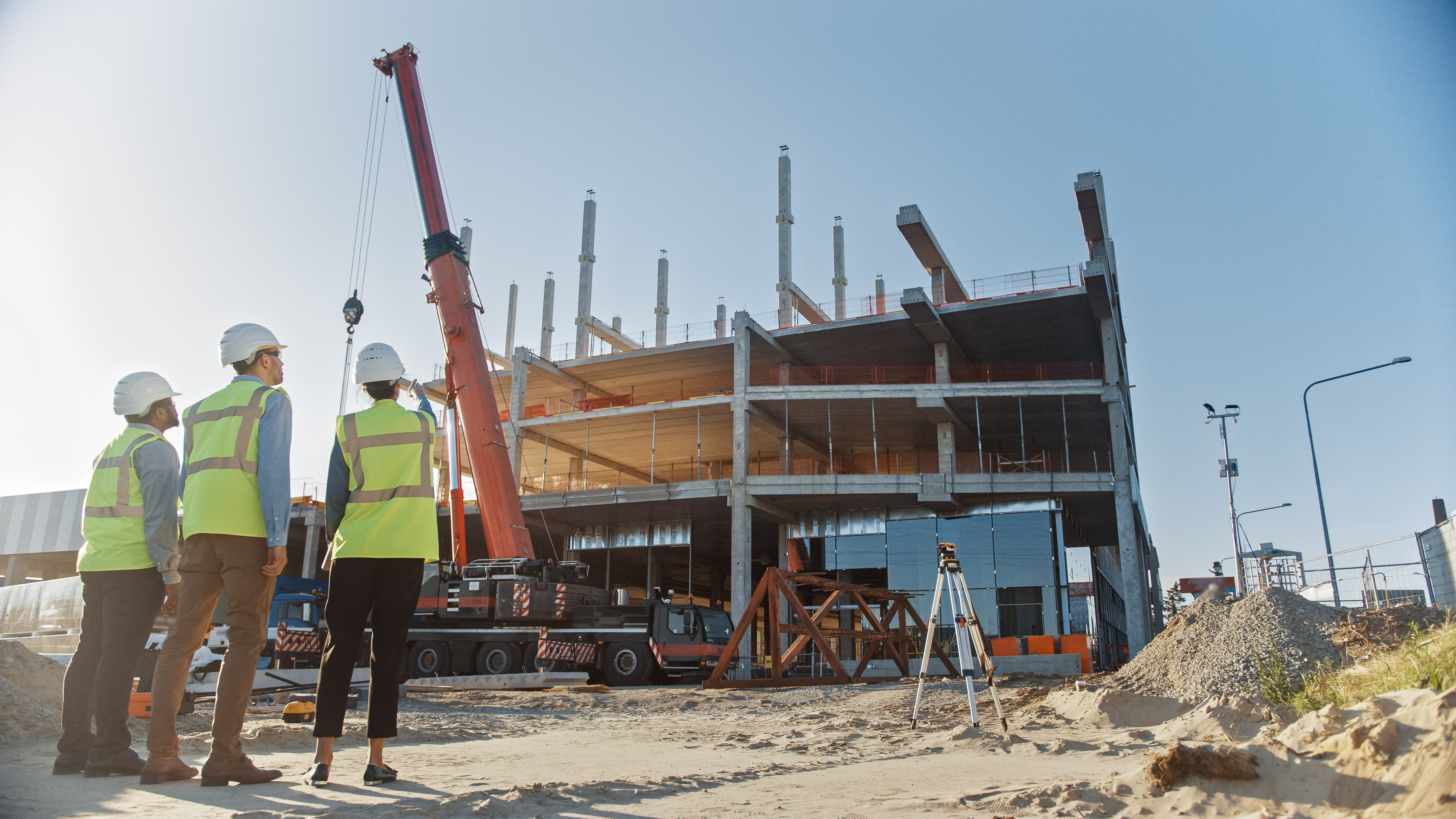 Construction workers survey a partially-constructed building with a crane in front of it.