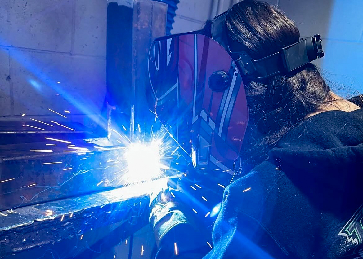 Woman welding metal with protective face shield