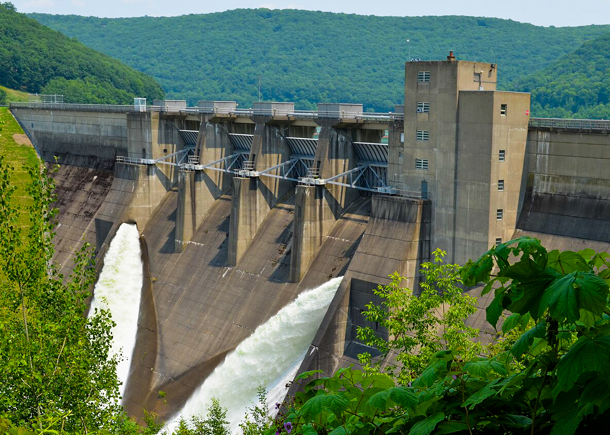 Large concrete dam releasing water in green valley