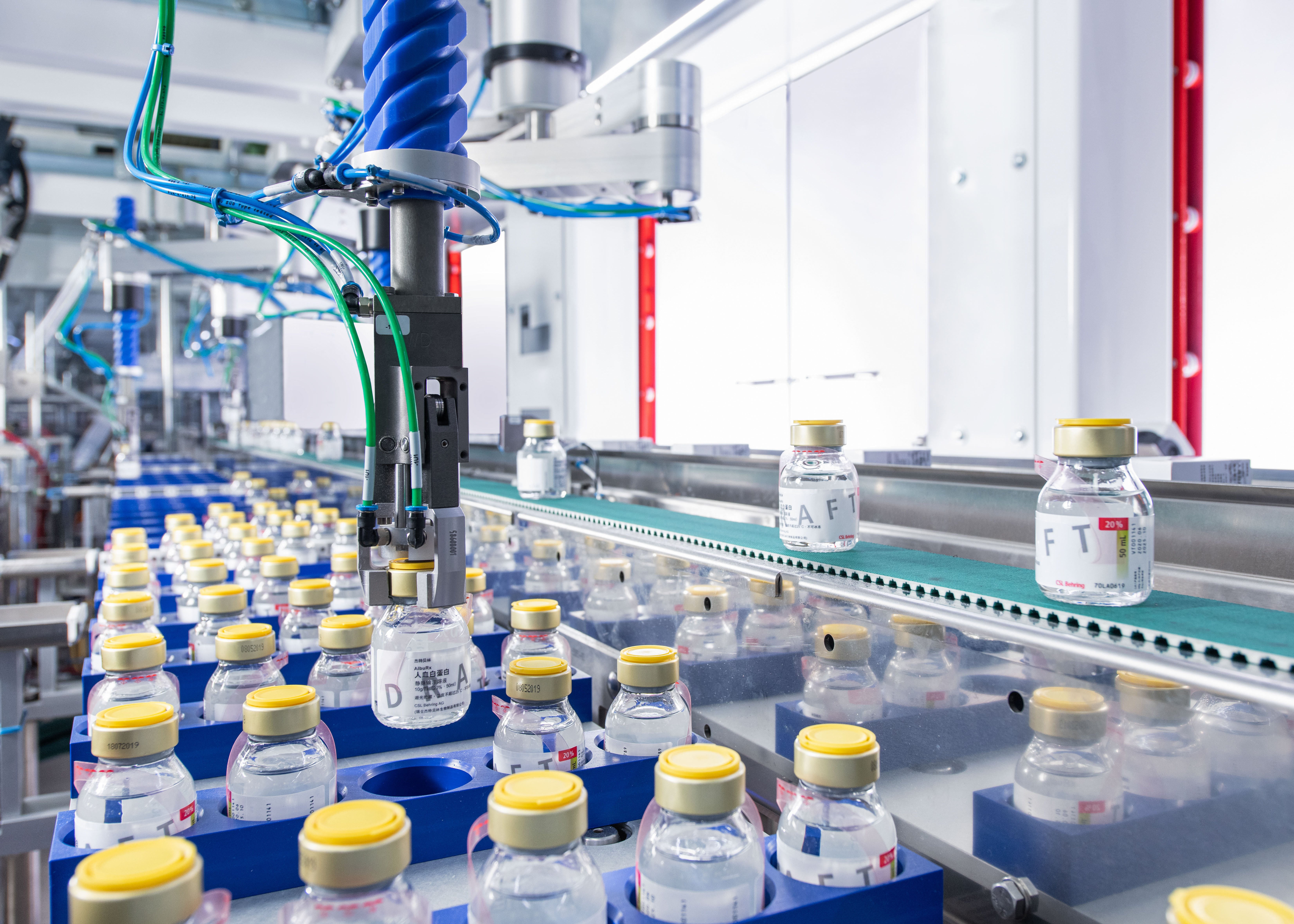 A robotic arm places vials of medicine on conveyor belt.