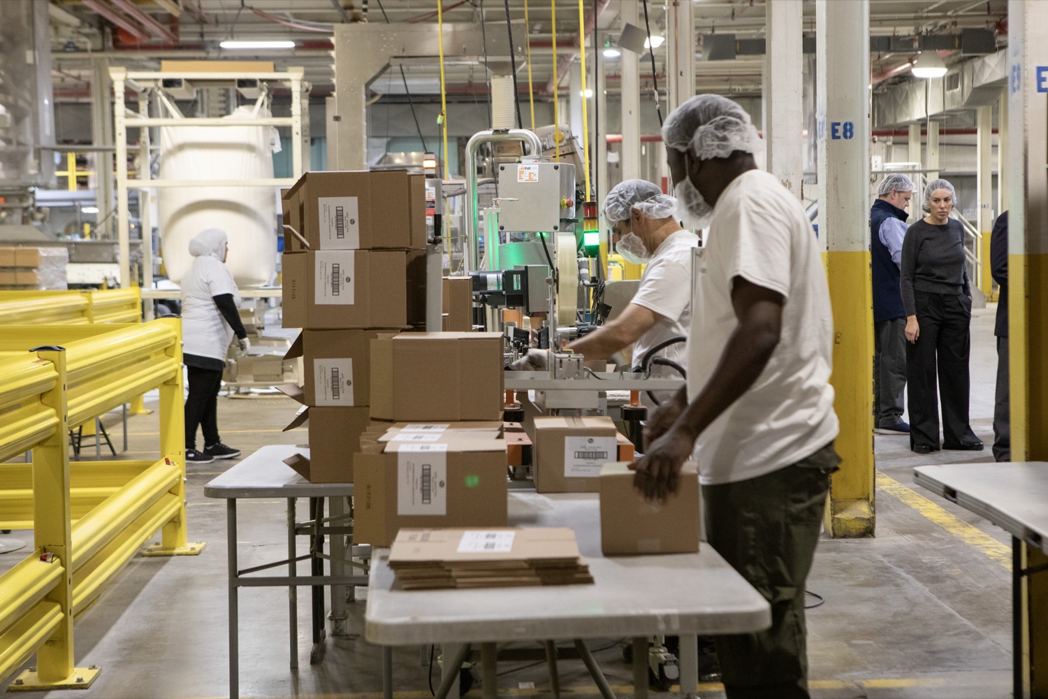 Employees package pouches of couscous into cardboard boxes in a manufacturing facility.