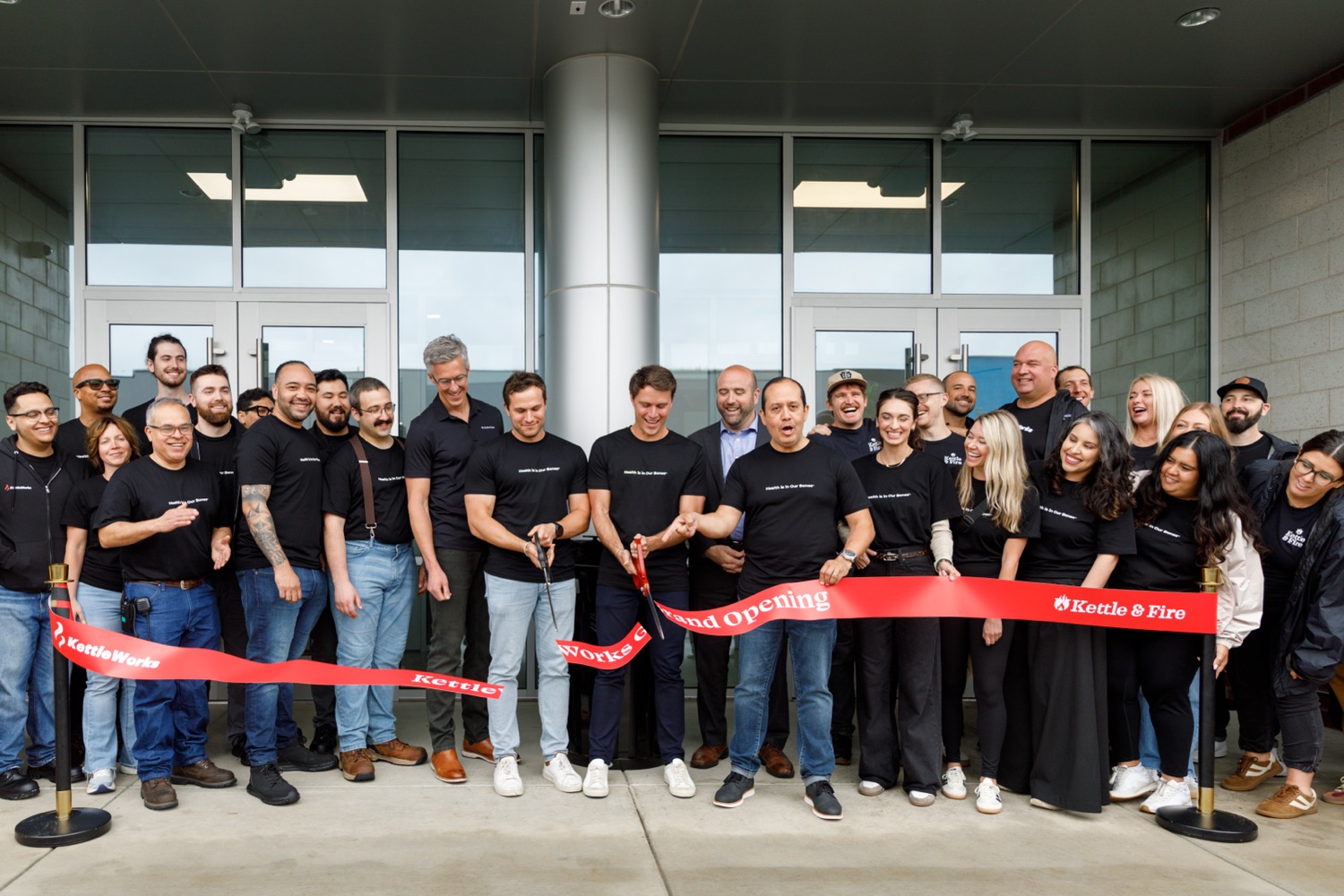 Pennsylvania Secretary Rick Siger and a large group of employees from the company Kettle & Fire cut a ribbon in front of a warehouse entrance.
