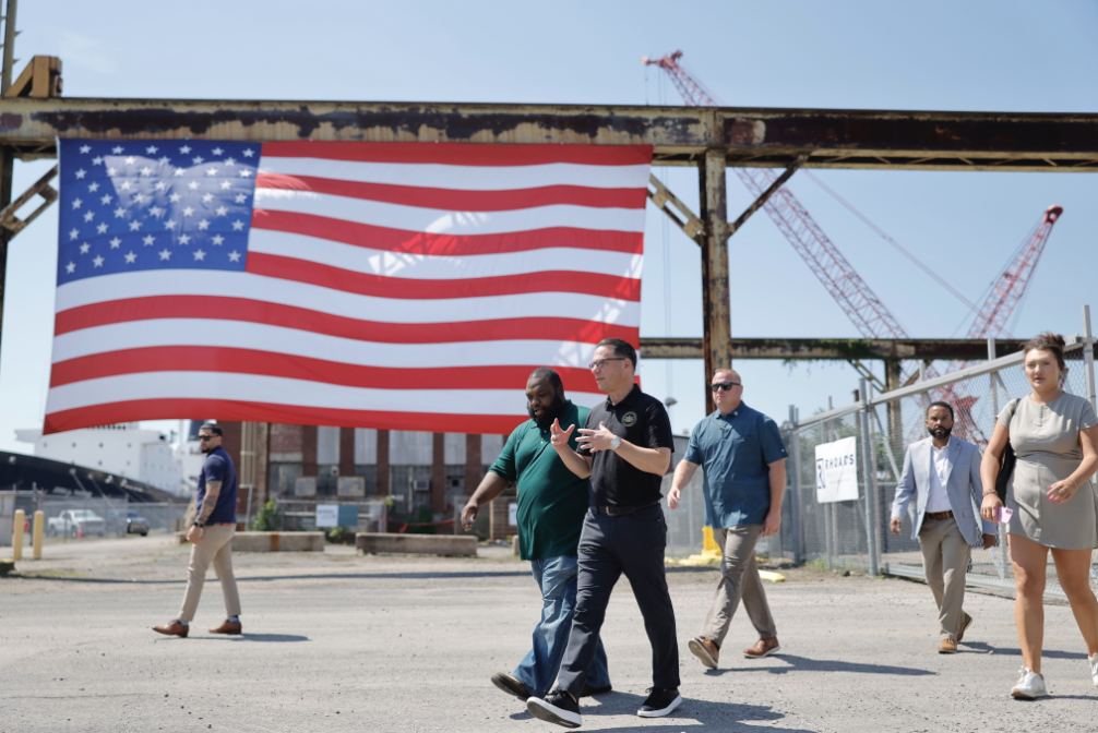 CEO of Rhoads Industries and Gov. Josh Shapiro walk through a construction site, with a large American flag in the background.