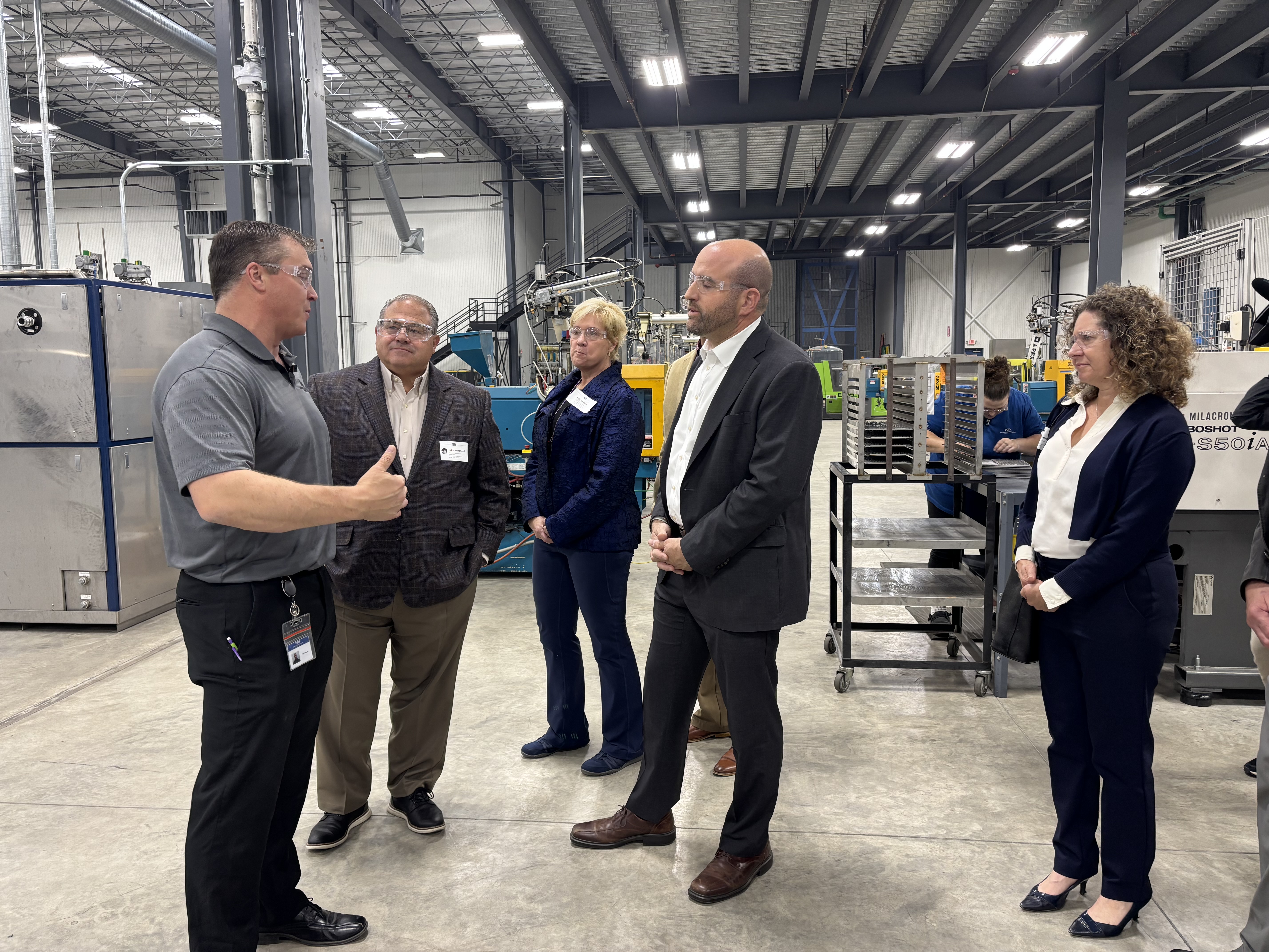 Secretary Rick Siger speaks with company officials in a large fabrication warehouse.