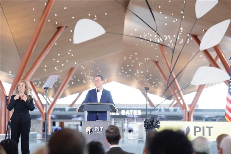 Governor Josh Shapiro speaks at a podium in the large new airport terminal at Pittsburgh International Airport