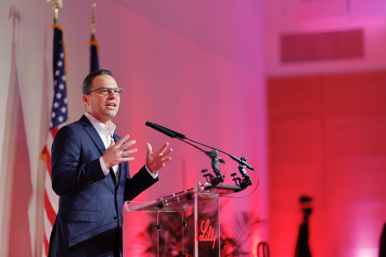 Governo Josh Shapiro speaks at a podium in a colorfully lit event hall.