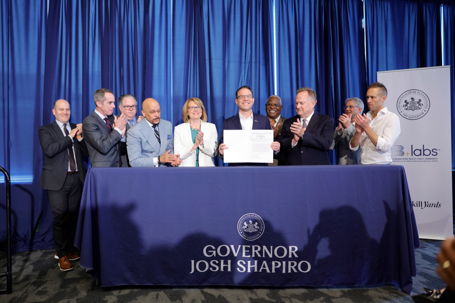 Governor Shapiro and a group of businesspeople smile as the Governor holds up a signed proclamation.
