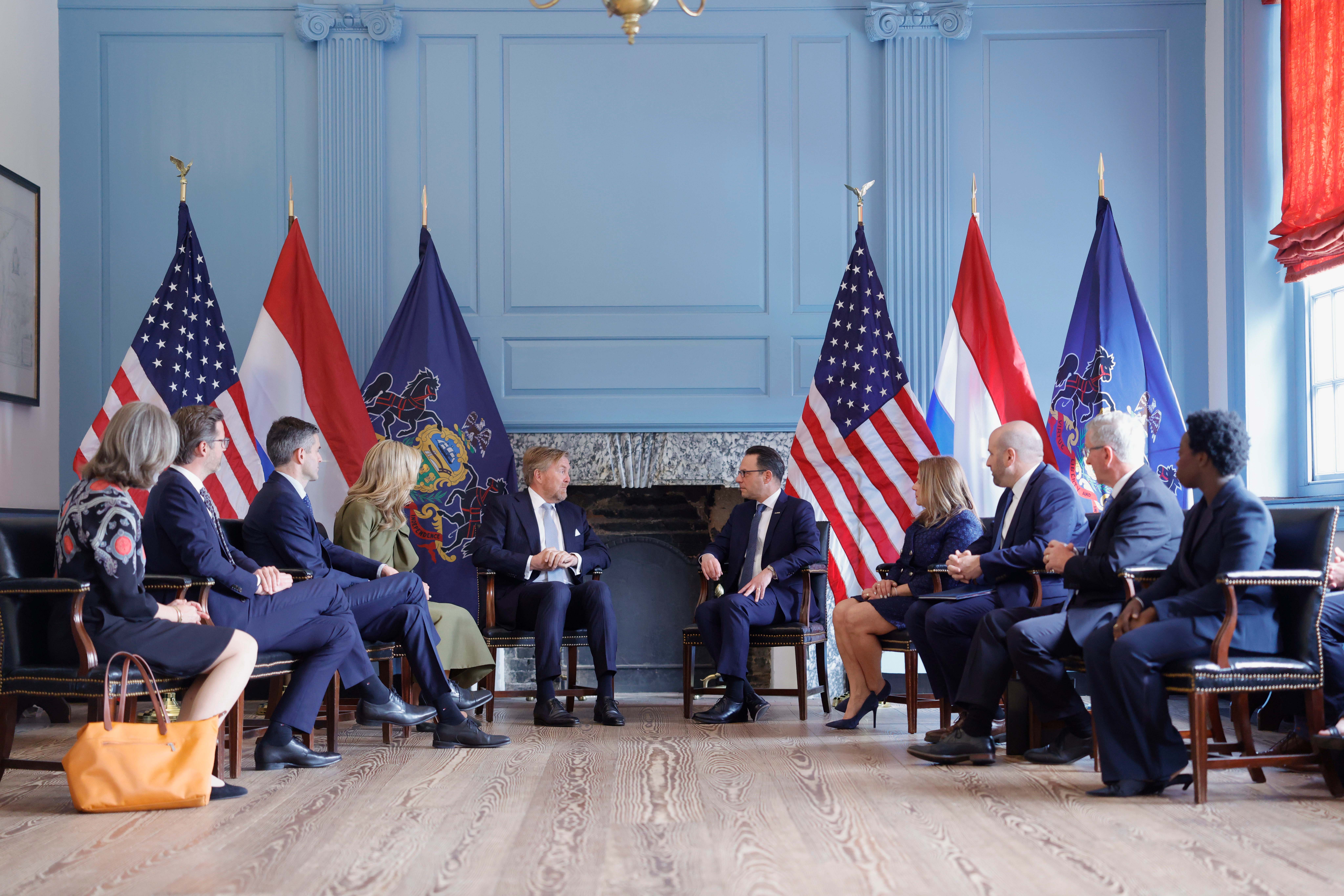 Governor Shapiro greets the Dutch King and Queen in a ballroom in front of a row of international flags