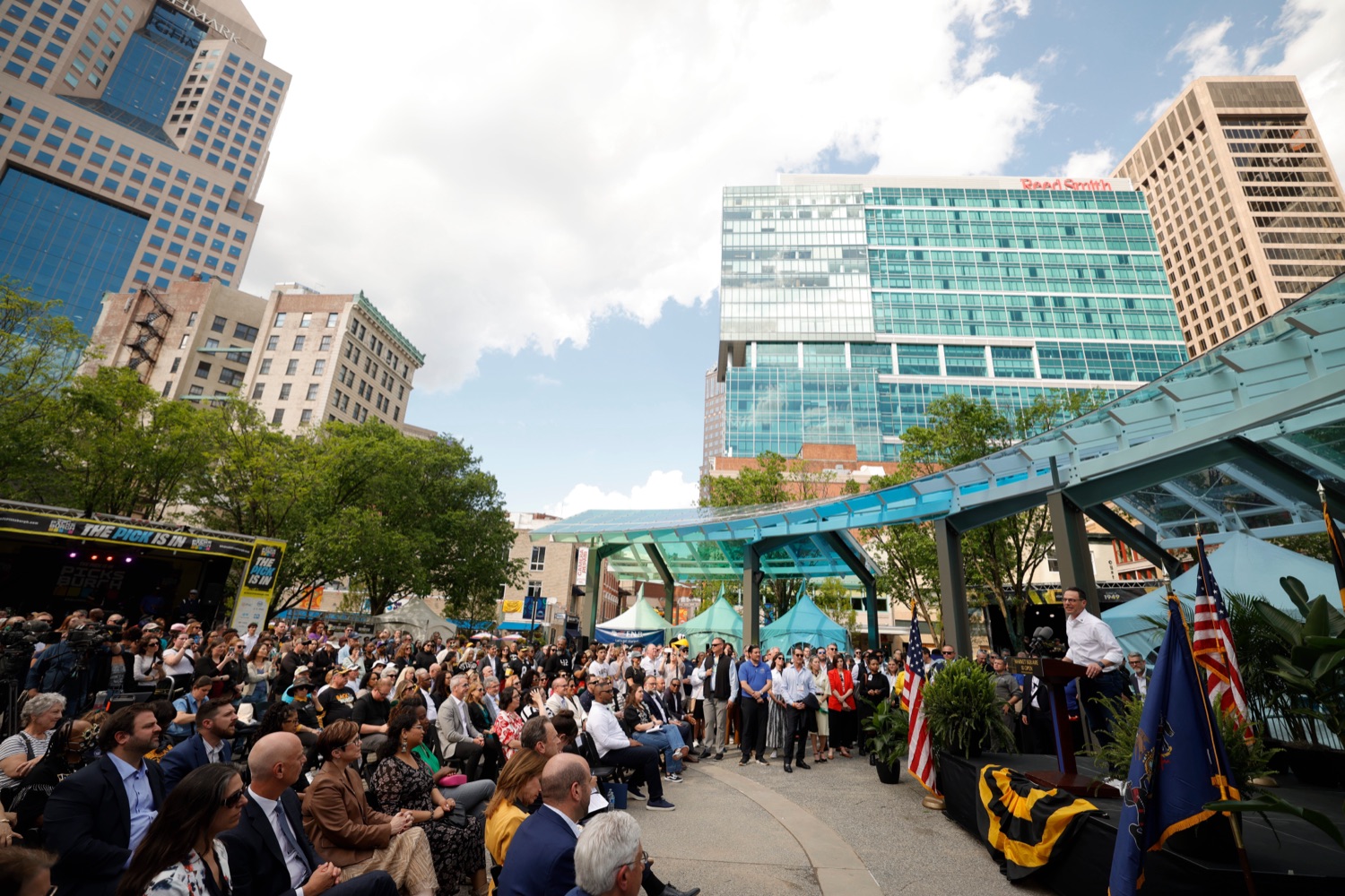 A large crowd sits in a plaza in Downtown Pittsburgh as Governor Josh Shapiro speak at a podium