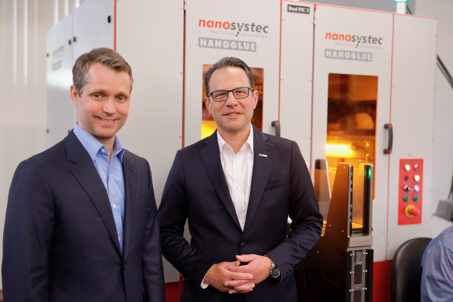 Governor Josh Shapiro poses for a photo with a business executive in front of a piece of advanced semiconductor manufacturing equipment.