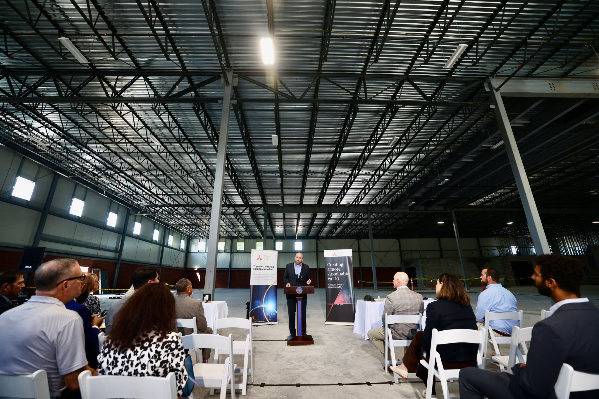 DCED Secretary Rick Siger speaks a podium to a small group of businesspeople. They are in a large, empty industrial warehouse.