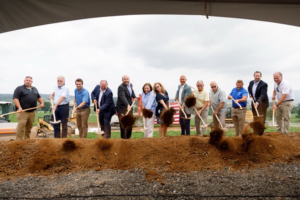  A group of government and business leaders participate in a ceremonial groundbreaking, shoveling dirt at a construction site.