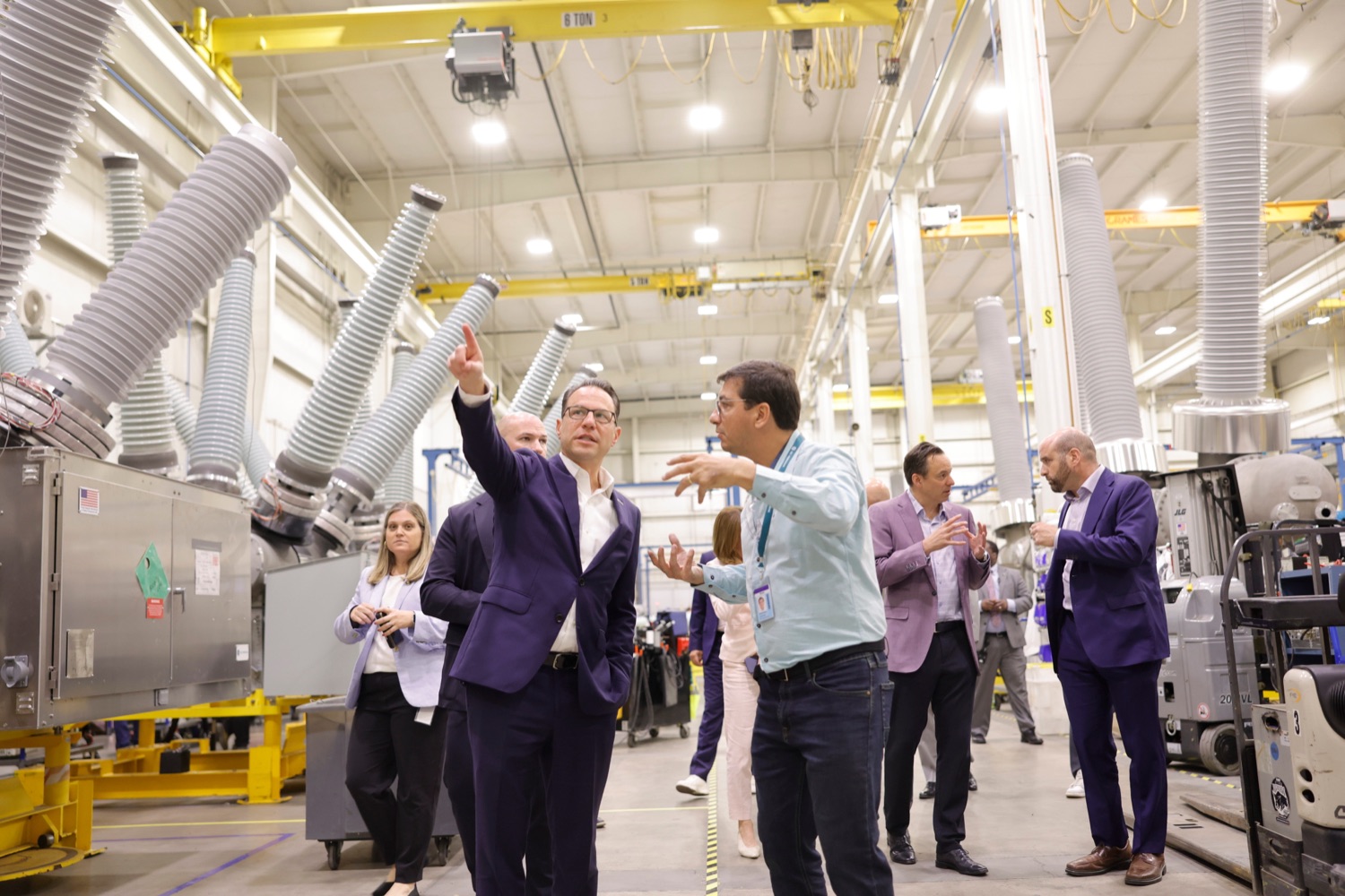 Governor Josh Shapiro speaks with a businessperson in an industrial facility during a press tour. A large electrical transformer is visible behind them.
