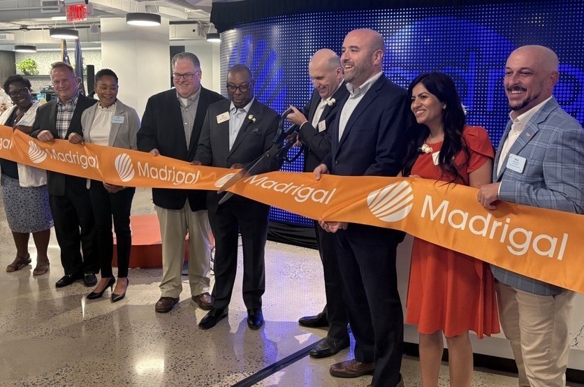 A group of businesspeople cut a ceremonial ribbon in an office interior.