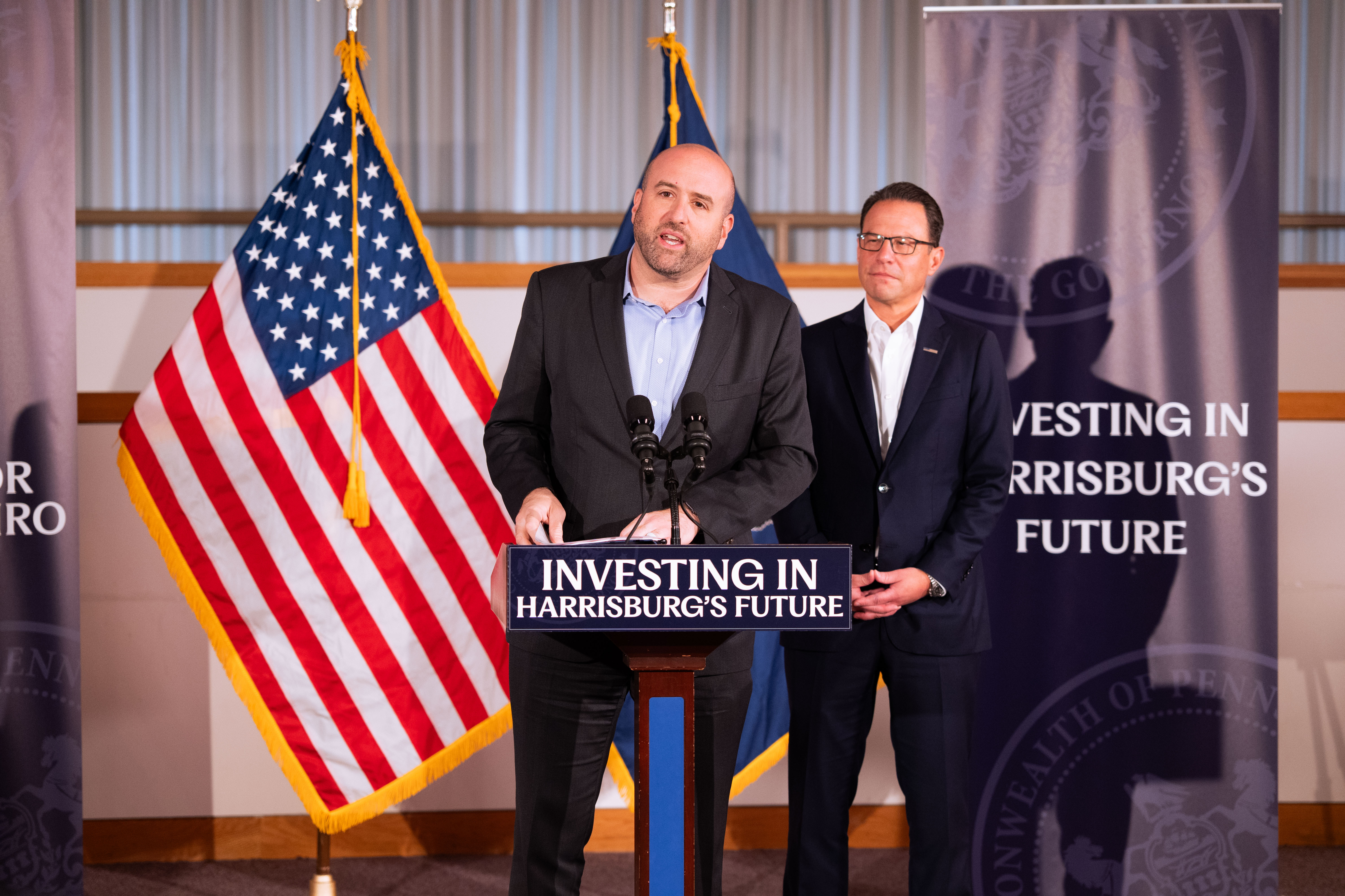 DCED Secretary Rick Siger speaks at a podium. Governor Josh Shapiro stands behind him. A sign reads: Investing in Harrisburg's Future