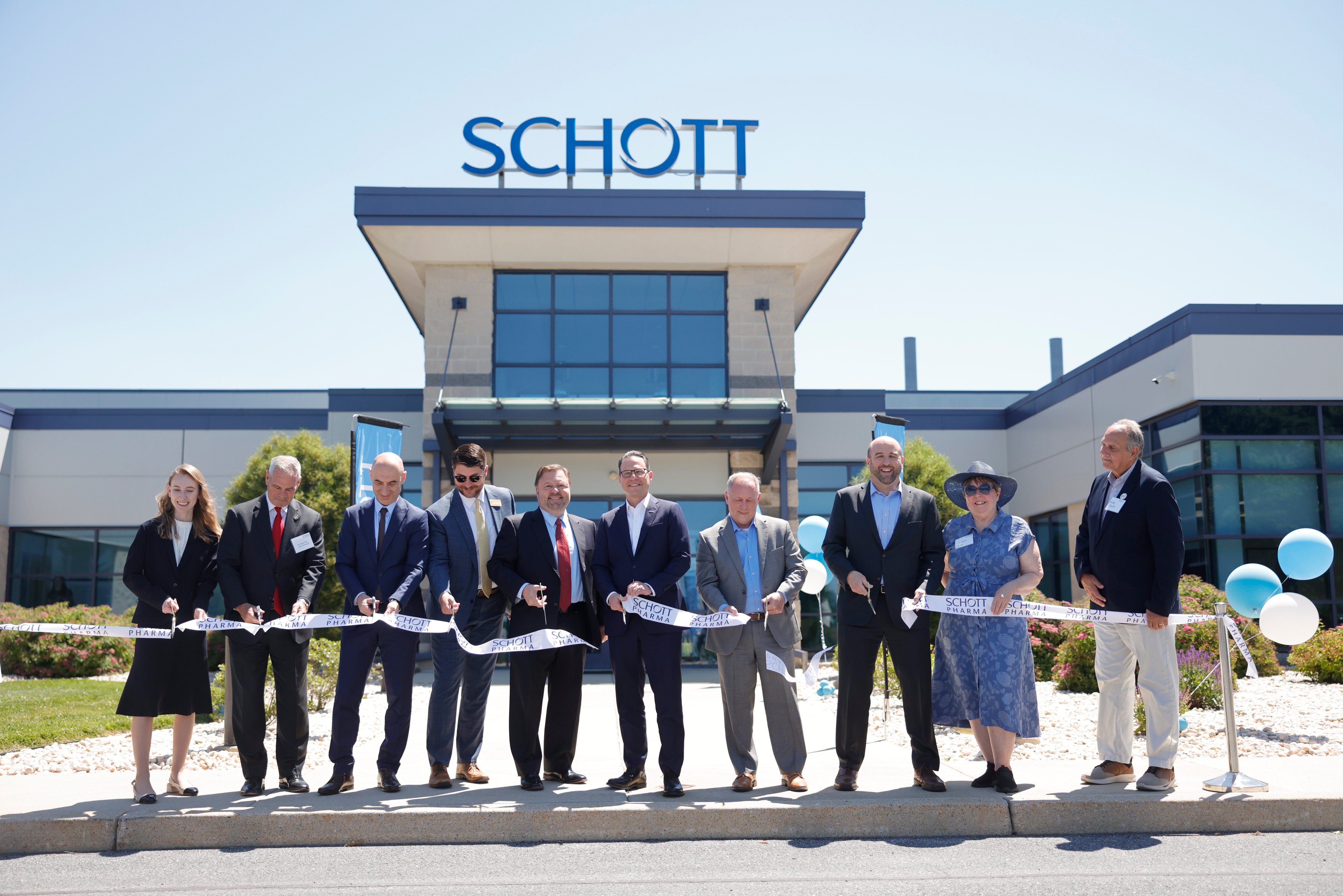 Governor Josh Shapiro and a group of government officials and businesspeople cut a ceremonial ribbon outside a corporate building for the company Schott.