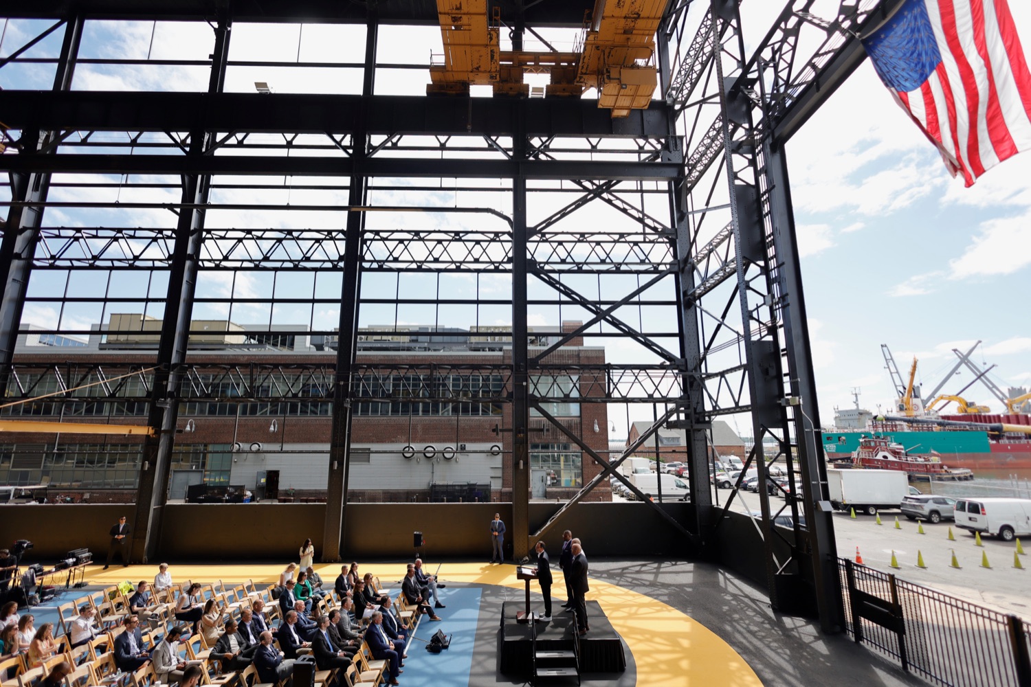 A person speaks at a podium in a large, partially built steel structure.