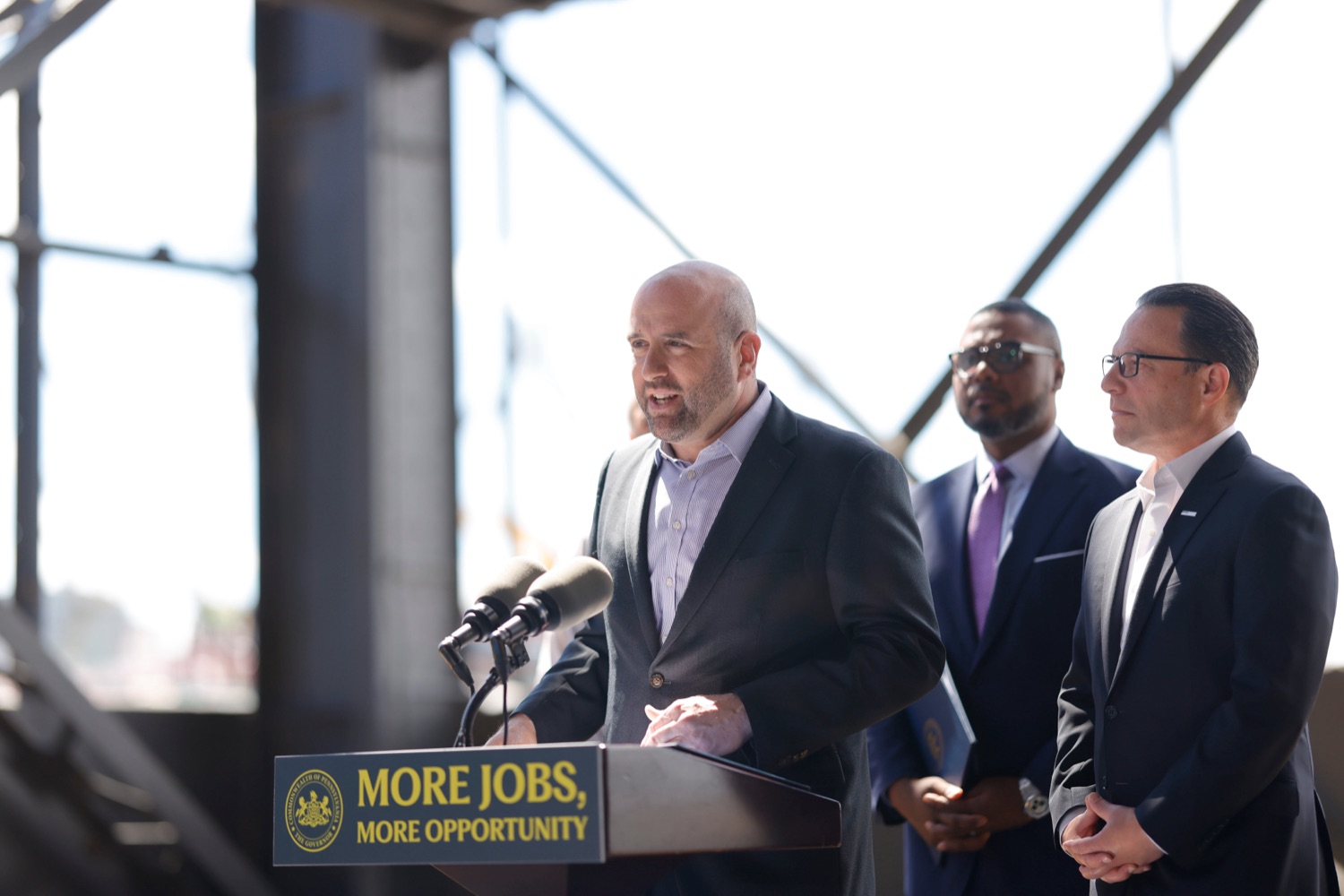 DCED Secretary Rick Siger, Governor Josh Shapiro, and Lieutenant Gov. Austin Davis stand near a podium.
