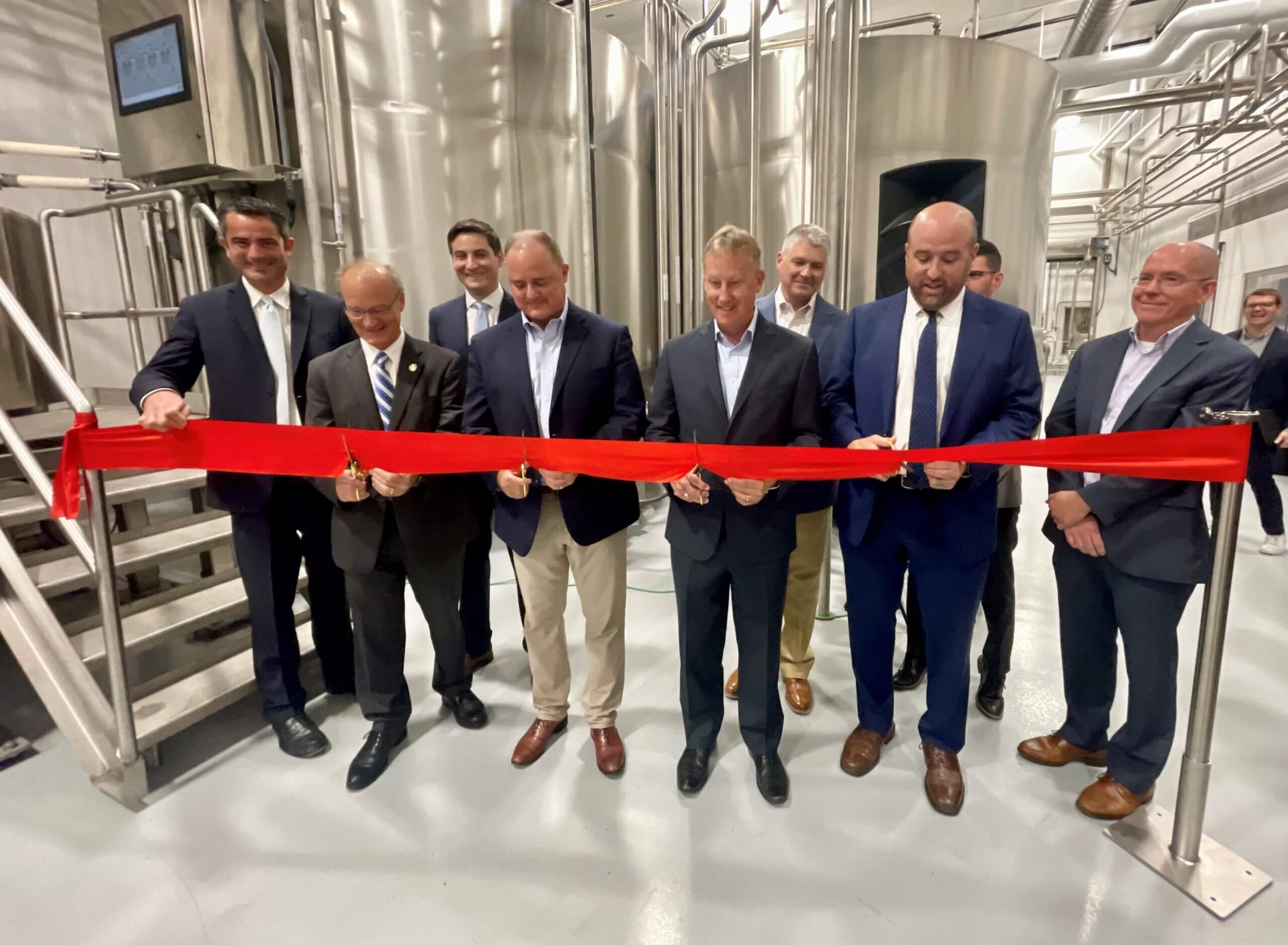 A ribbon cutting event in a sleek industrial warehouse, with shiny tubes and metal silos in the background.