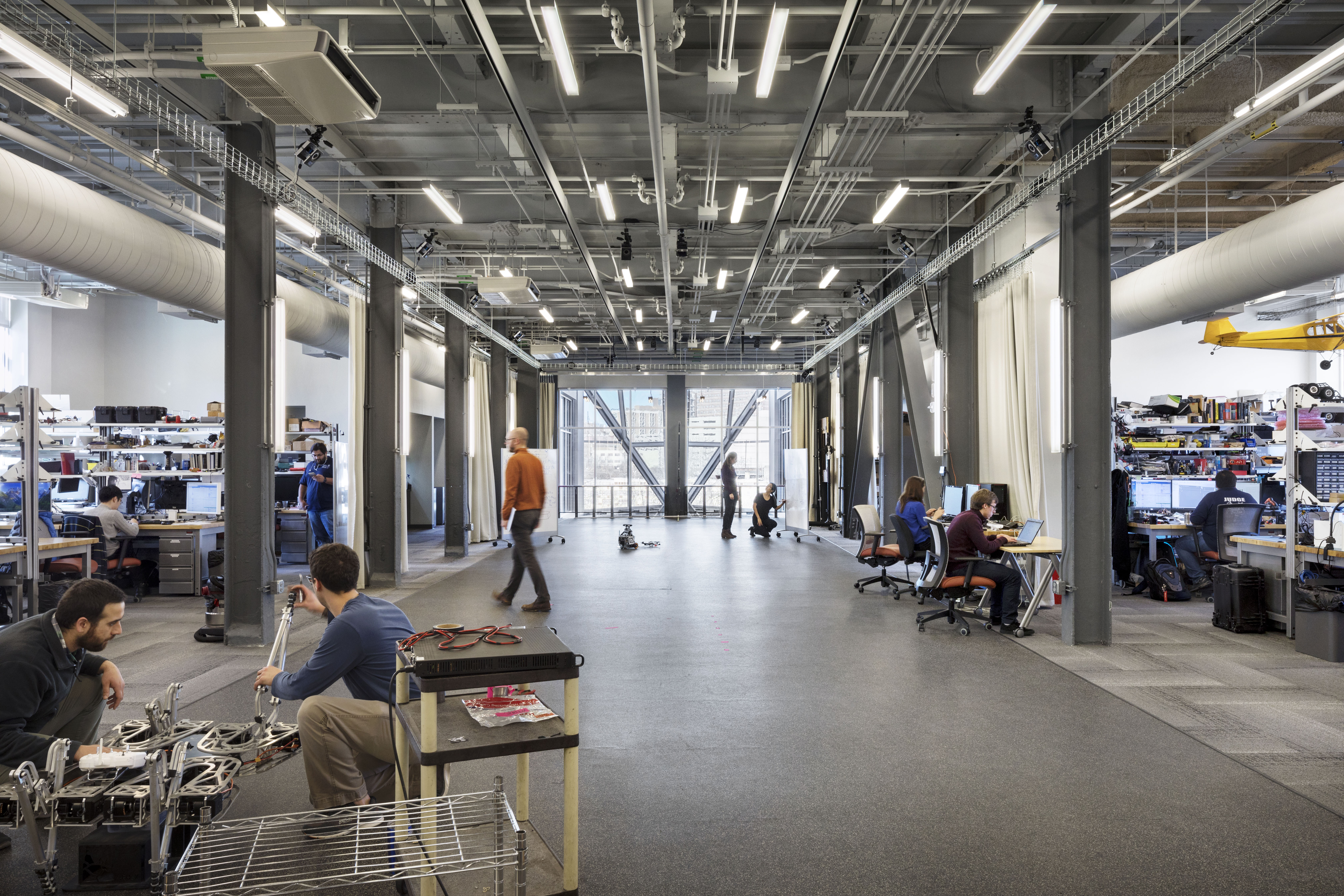 An industrial, modern office space with a few people mingling in the background