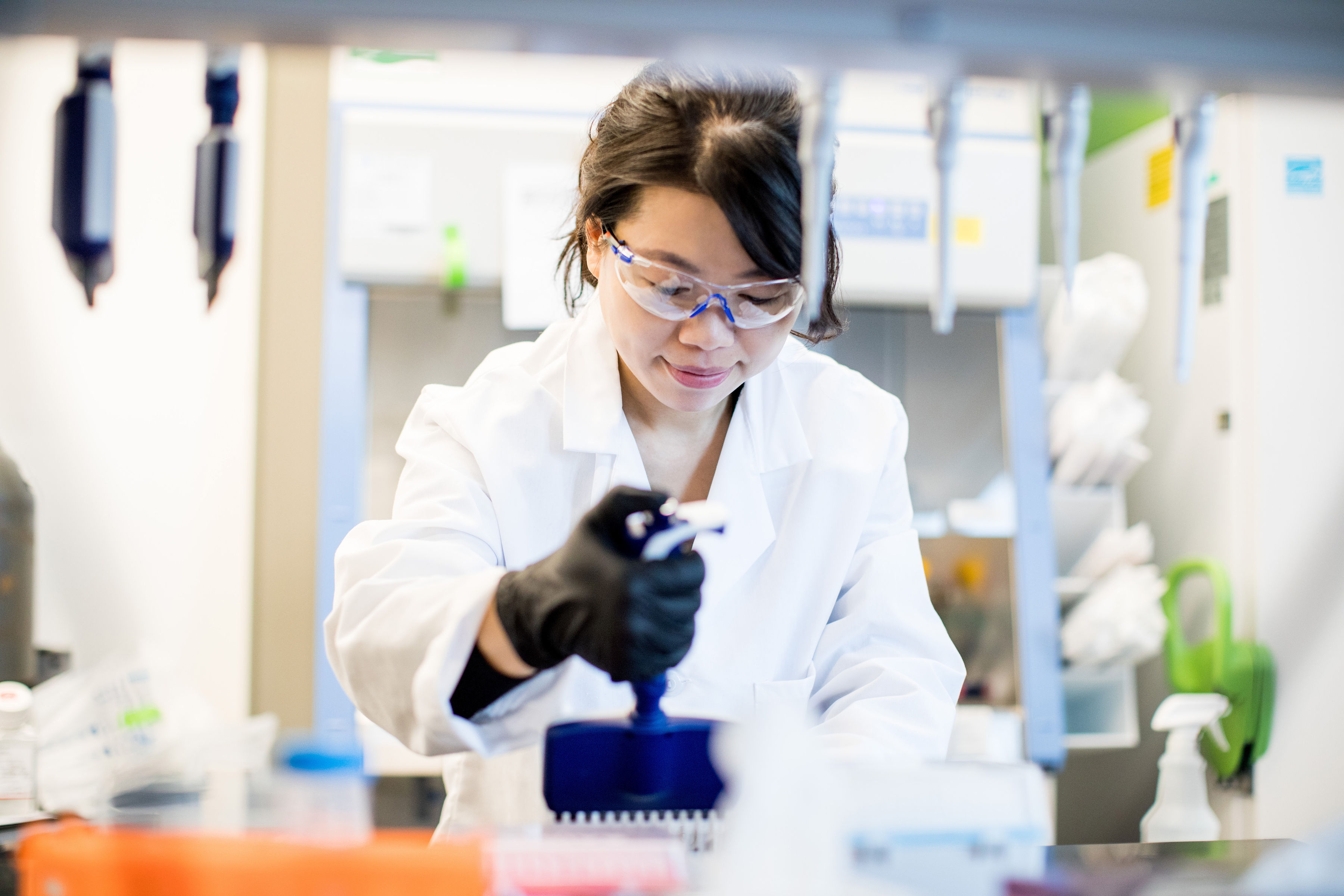A scientist wearing a labcoat and safety goggles works in a clean room lab space